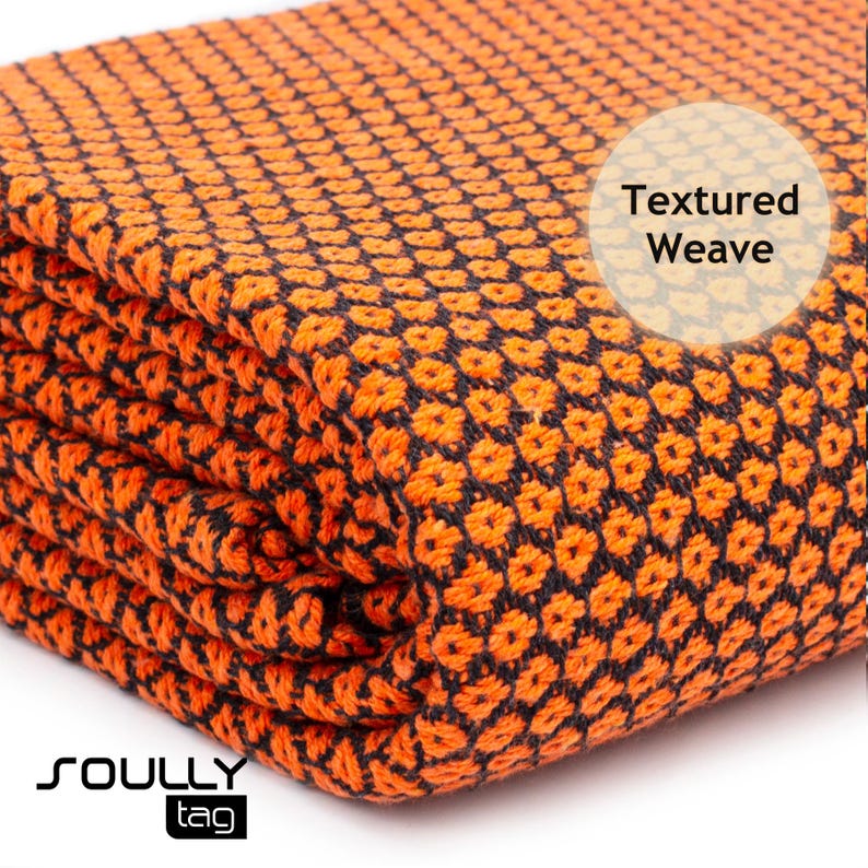 May include: Folded orange and black textured weave fabric. The fabric has a repeating pattern of small, raised squares. The words "Textured Weave" are in a white circle. The brand name "SOULLY" and the word "tag" are in the bottom left corner.