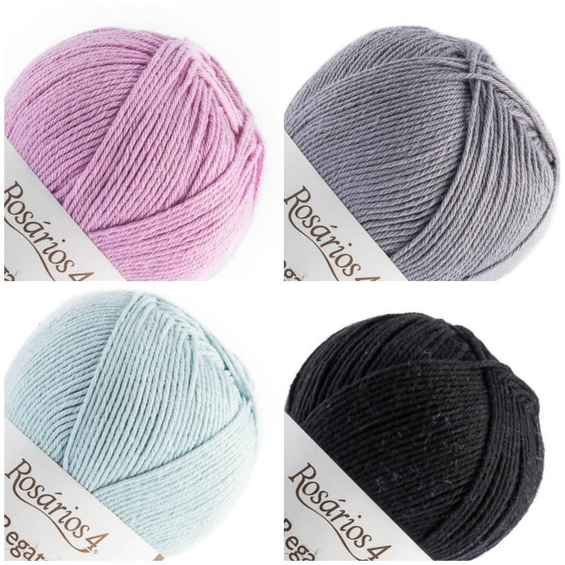 May include: Four round balls of yarn in light pink, grey, light blue, and black. Each ball features a white paper label with the text Ros&aacute;rios 4 printed in black. The yarn is wound in a smooth, consistent pattern, showing the texture of the fiber.