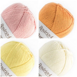 May include: Four balls of yarn in pastel pink, orange, light yellow, and cream. Each ball features a white paper band with the text Ros&aacute;rios 4 printed in black. The yarn is wound into a round shape, displaying a smooth, twisted fiber texture.