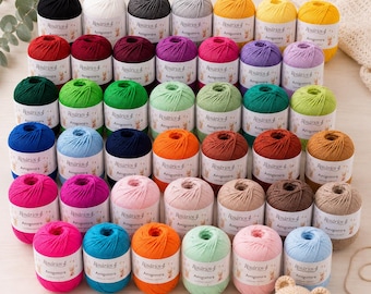 May include: A collection of Rosários 4 Amigomira yarn balls in various solid colours, each with a white label. A red crochet hook with 3.5 mm printed on the handle and a small crocheted bear head are placed in front of the yarn assortment.