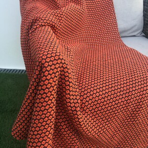 May include: An orange and black patterned throw blanket draped over a chair. The blanket features a repeating floral design. The color palette is a warm orange and black, creating a cozy and inviting aesthetic. The blanket is made of a soft, textured material.