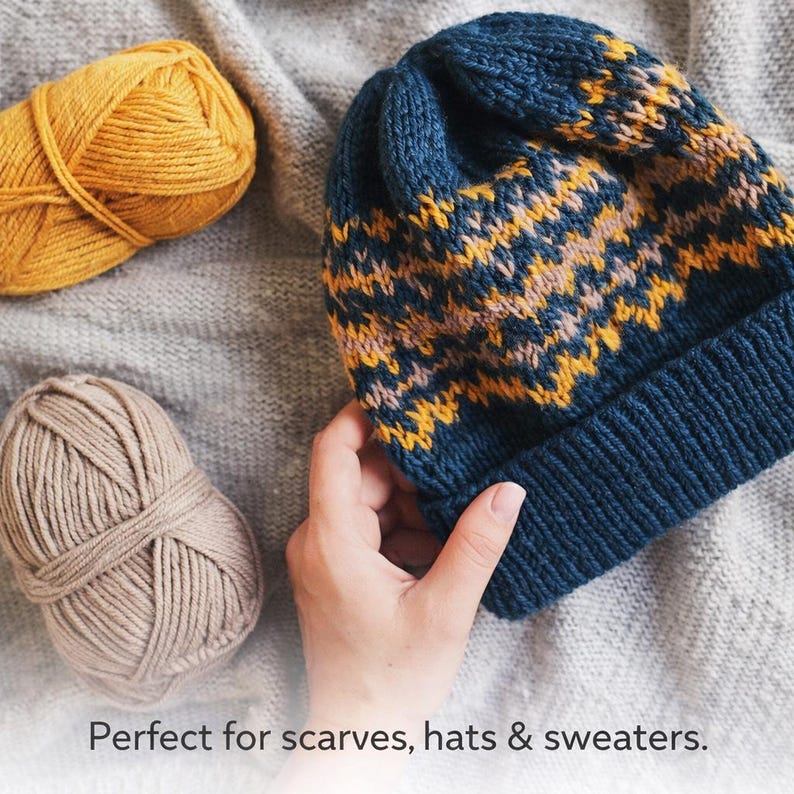 May include: A knitted beanie featuring a navy blue, mustard yellow, and light pink zigzag pattern with a ribbed cuff, accompanied by a mustard yellow yarn ball and a beige yarn ball, with text reading: Perfect for scarves, hats & sweaters.