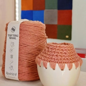 May include: A skein of pink yarn labeled "Tufting Wool" by "Rosarios 4."  The yarn is next to a white ceramic yarn bowl with a crocheted pink lid.