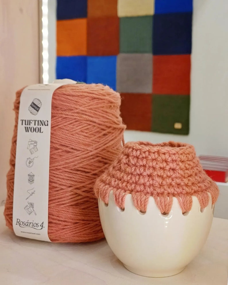 May include: A skein of pink yarn labeled "Tufting Wool" by "Rosarios 4."  The yarn is next to a white ceramic yarn bowl with a crocheted pink lid.