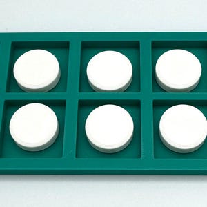 May include: A rectangular teal ten-frame math manipulative tray with ten square compartments. The text "Ten Frame" is printed in white on the left side. Ten solid white circular counters are placed inside each of the individual square slots.