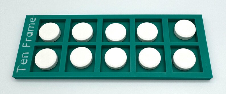 May include: A rectangular teal ten-frame math manipulative tray with ten square compartments. The text "Ten Frame" is printed in white on the left side. Ten solid white circular counters are placed inside each of the individual square slots.