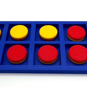 May include: A blue rectangular ten frame math manipulative tray with the text Ten Frame printed in white. The tray contains three yellow circular counters in the top row and seven red circular counters filling the remaining slots in the grid.
