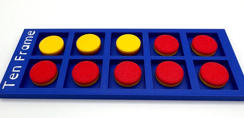 May include: A blue rectangular ten frame math manipulative tray with the text Ten Frame printed in white. The tray contains three yellow circular counters in the top row and seven red circular counters filling the remaining slots in the grid.