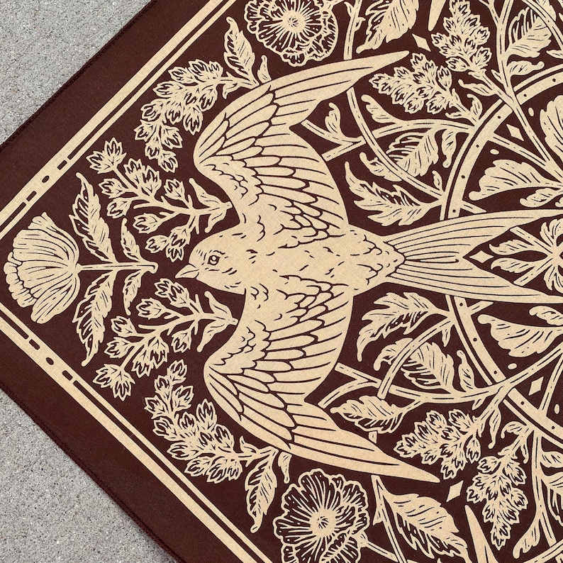 May include: A brown bandana with a white bird and floral design. The bird is flying with its wings spread out. The flowers are in bloom and have intricate details.
