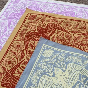 May include: Three fabric bandanas with different floral and bird designs. The top bandana is white with purple flowers and birds. The middle bandana is beige with red birds and flowers. The bottom bandana is blue with yellow birds and flowers.