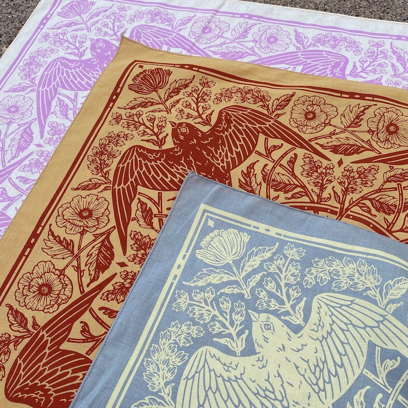 May include: Three fabric bandanas with different floral and bird designs. The top bandana is white with purple flowers and birds. The middle bandana is beige with red birds and flowers. The bottom bandana is blue with yellow birds and flowers.