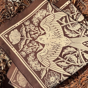 May include: A brown fabric square with a white bird and floral design. The bird is in flight and has a long tail. The flowers are stylized and have a vintage look.