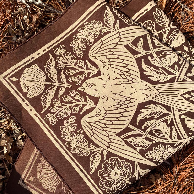 May include: A brown fabric square with a white bird and floral design. The bird is in flight and has a long tail. The flowers are stylized and have a vintage look.