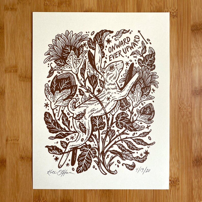 Pu&ograve; includere: Una stampa linoleografica in marrone e bianco di un coniglio che salta in alto attraverso un campo di fiori. Il testo "Onward Ever Upward!" &egrave; scritto nell'angolo in alto a destra della stampa. La stampa &egrave; firmata "Katie Offner" e datata "4/19/20".
