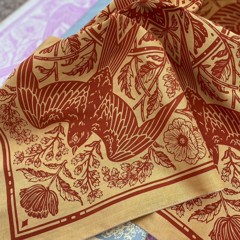 May include: A tan bandana with a red bird and floral pattern. The bird is flying with its wings spread wide. The floral pattern includes flowers and leaves.