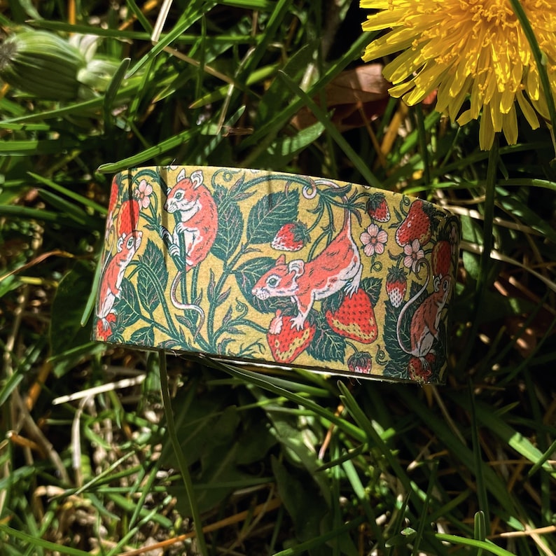 May include: A roll of washi tape with a repeating pattern of red strawberries, green leaves, and small brown mice on a yellow background.