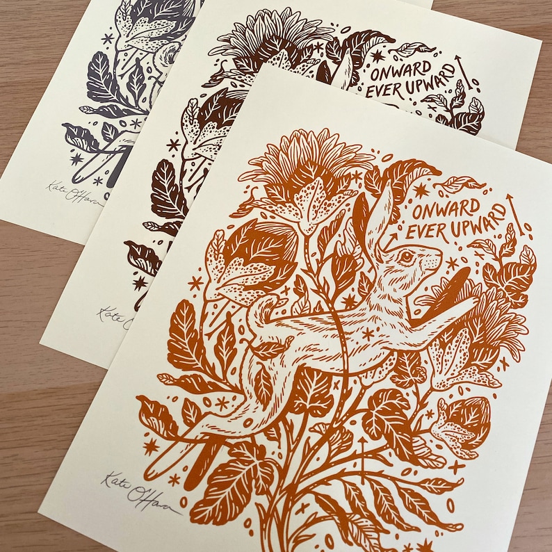 Pu&ograve; includere: Una stampa in linoleum marrone e bianco di un coniglio che salta attraverso un campo di fiori. La stampa ha uno sfondo bianco e il testo "ONWARD EVER UPWARD" &egrave; scritto in un carattere stilizzato.
