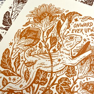 Pu&ograve; includere: Un'illustrazione marrone e bianca di un coniglio che corre attraverso un campo di fiori. Il coniglio &egrave; circondato da foglie e fiori. Il testo "ONWARD EVER UPWARD" &egrave; scritto in un font stilizzato sopra il coniglio.