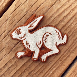 May include: White embroidered rabbit patch with brown outline, ideal for adding a whimsical touch to clothing, bags, or crafts.