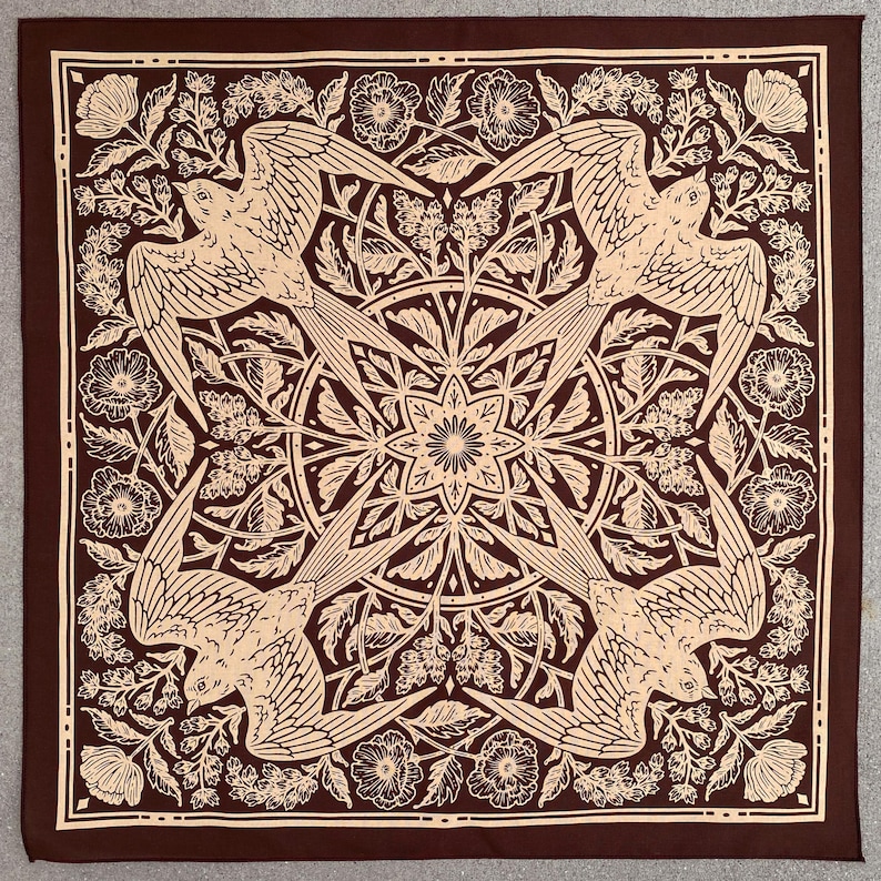 May include: A brown bandana with a tan design of four birds flying in a circle, surrounded by floral patterns. The birds are stylized and have a geometric look.