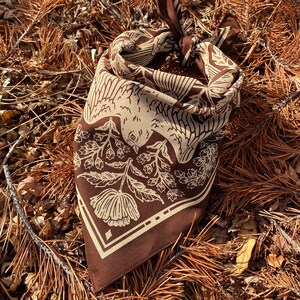 May include: A brown bandana with a white floral and bird design. The bandana is folded and tied in a knot.
