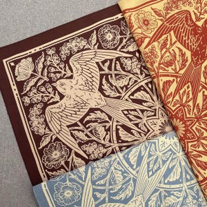 May include: Three fabric squares with a repeating pattern of stylized birds and floral designs. The squares are in shades of brown, red, and blue.