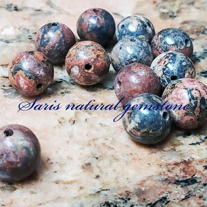 Peut inclure: Une collection de 10 perles rondes en pierres pr&eacute;cieuses tachet&eacute;es de rouge, de bleu et de blanc. Les perles mesurent environ 2,5 cm de diam&egrave;tre et ont un trou perc&eacute; au centre.
