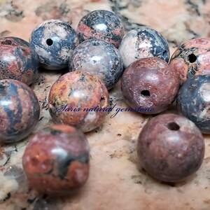 Peut inclure: Un ensemble de 12 perles rondes en pierres pr&eacute;cieuses naturelles multicolores avec des trous perc&eacute;s au centre. Les perles sont un m&eacute;lange de rouge, brun, noir et blanc.