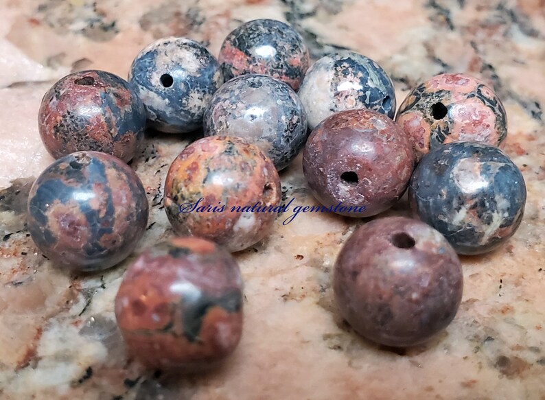 Peut inclure: Un ensemble de 12 perles rondes en pierres pr&eacute;cieuses naturelles multicolores avec des trous perc&eacute;s au centre. Les perles sont un m&eacute;lange de rouge, brun, noir et blanc.