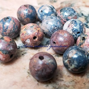 Peut inclure: Une collection de 12 perles rondes en pierres pr&eacute;cieuses naturelles, multicolores et tachet&eacute;es, avec des trous perc&eacute;s au centre. Les perles mesurent environ 2,5 cm de diam&egrave;tre et pr&eacute;sentent une vari&eacute;t&eacute; de couleurs, notamment le rose, le rouge, le bleu, le vert et le noir.