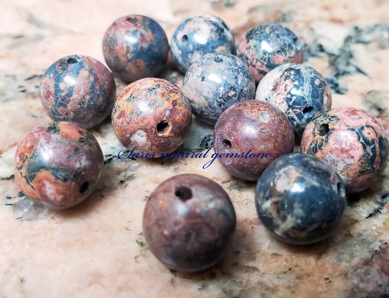 Peut inclure: Une collection de 12 perles rondes en pierres pr&eacute;cieuses naturelles, multicolores et tachet&eacute;es, avec des trous perc&eacute;s au centre. Les perles mesurent environ 2,5 cm de diam&egrave;tre et pr&eacute;sentent une vari&eacute;t&eacute; de couleurs, notamment le rose, le rouge, le bleu, le vert et le noir.