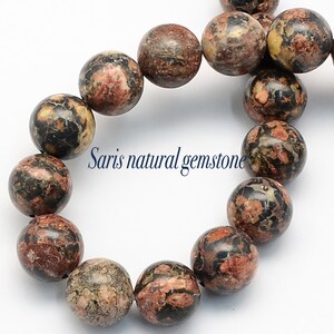 Peut inclure: Un brin de perles rondes en pierre pr&eacute;cieuse mouchet&eacute;es de brun, de noir et de rouge. Les perles mesurent environ 10 mm de diam&egrave;tre. Les perles sont enfil&eacute;es sur un cordon &eacute;lastique transparent.