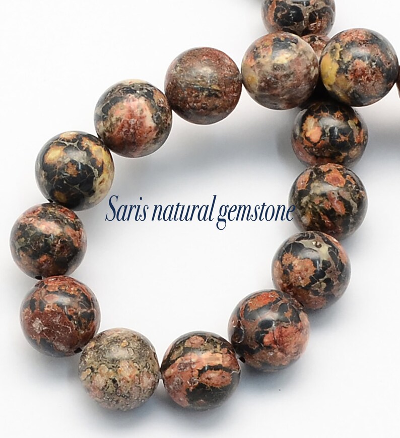 Peut inclure: Un brin de perles rondes en pierre pr&eacute;cieuse mouchet&eacute;es de brun, de noir et de rouge. Les perles mesurent environ 10 mm de diam&egrave;tre. Les perles sont enfil&eacute;es sur un cordon &eacute;lastique transparent.