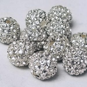 Puede incluir: Un conjunto de cuentas redondas de color plateado incrustadas con brillantes pedrer&iacute;a. Las cuentas est&aacute;n agrupadas, mostrando sus superficies reflectantes. Estas cuentas decorativas son ideales para la fabricaci&oacute;n de joyas y proyectos de artesan&iacute;a.