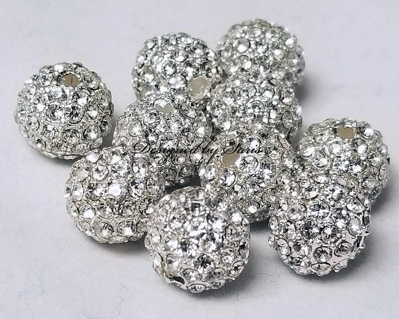 Puede incluir: Un conjunto de cuentas redondas de color plateado incrustadas con brillantes pedrer&iacute;a. Las cuentas est&aacute;n agrupadas, mostrando sus superficies reflectantes. Estas cuentas decorativas son ideales para la fabricaci&oacute;n de joyas y proyectos de artesan&iacute;a.