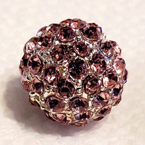 Puede incluir: Una cuenta redonda y brillante con una base plateada y un grupo de peque&ntilde;os diamantes de imitaci&oacute;n de color p&uacute;rpura iridiscente.