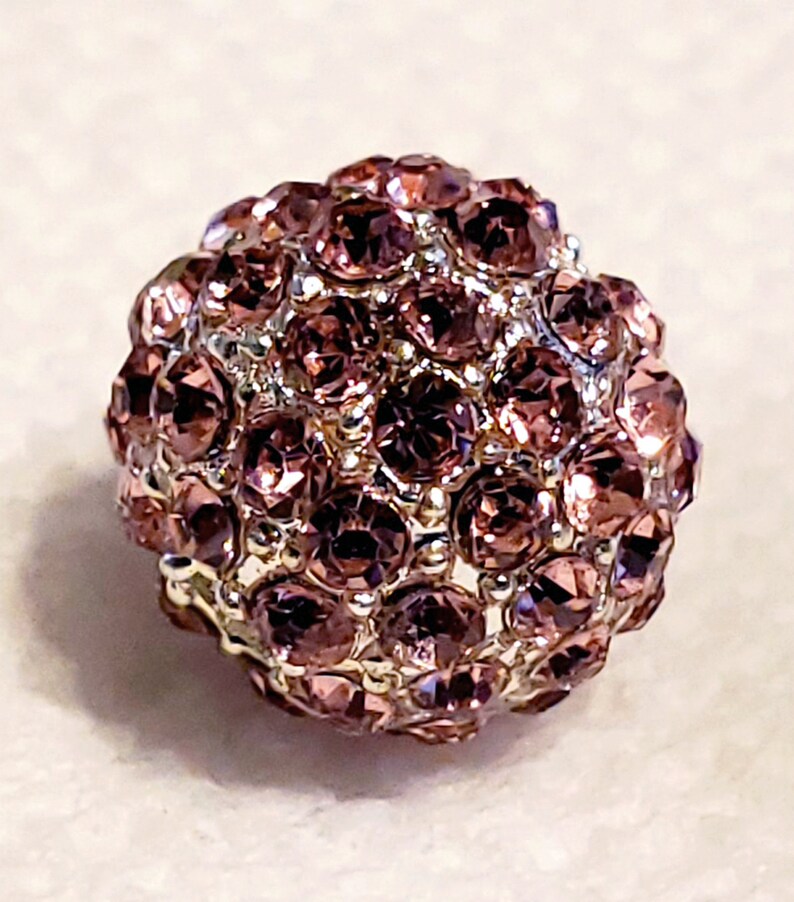 Puede incluir: Una cuenta redonda y brillante con una base plateada y un grupo de peque&ntilde;os diamantes de imitaci&oacute;n de color p&uacute;rpura iridiscente.