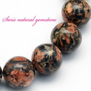 Peut inclure: Gros plan sur un bracelet compos&eacute; de perles rondes en pierre pr&eacute;cieuse mouchet&eacute;es de noir, de brun et de rouge. Les perles sont polies et ont un aspect naturel et organique.