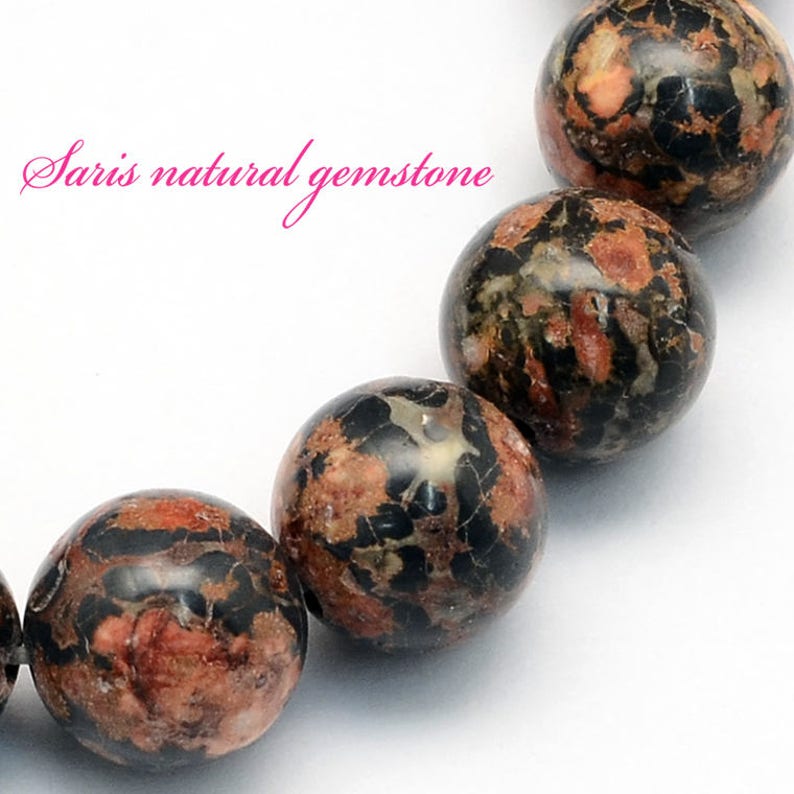 Peut inclure: Gros plan sur un bracelet compos&eacute; de perles rondes en pierre pr&eacute;cieuse mouchet&eacute;es de noir, de brun et de rouge. Les perles sont polies et ont un aspect naturel et organique.
