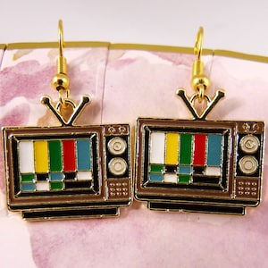 May include: Gold-tone earrings shaped like vintage televisions with a colourful test pattern on the screen.