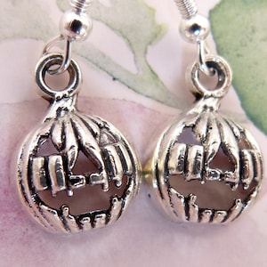 May include: A pair of silver pumpkin earrings with a carved jack-o'-lantern face. The earrings are dangle style with a silver hook.