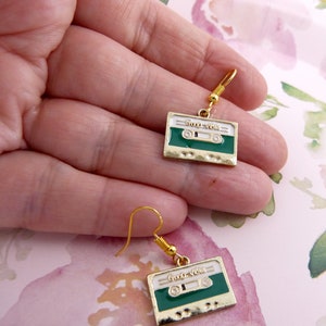 May include: A pair of gold tone earrings with green and white cassette tape charms. The charms have the text "Good Vibes" on them.