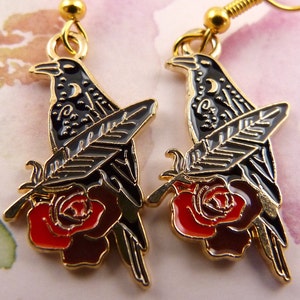 May include: Gold tone earrings featuring a black raven perched on a red rose with a gold feather.