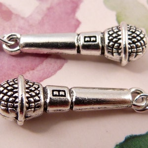Peut inclure: Une paire de boucles d'oreilles en argent en forme de microphone. Chaque boucle d'oreille présente un petit charme de microphone détaillé avec une surface texturée et une boucle en argent pour accrocher.