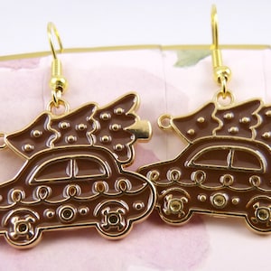Peut inclure: Une paire de boucles d'oreilles dorées représentant une voiture marron avec un sapin de Noël sur le toit. La voiture présente des détails décoratifs et est suspendue à un crochet doré. Ces boucles d'oreilles sont conçues pour les fêtes.