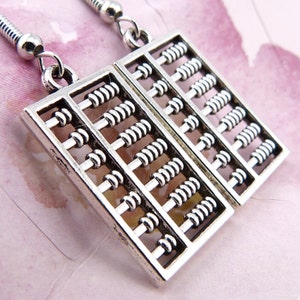 May include: Silver abacus earrings with a rectangular shape. The abacus beads are silver and are arranged in rows.