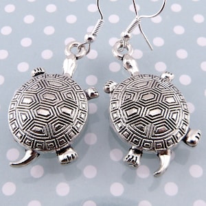 May include: Silver turtle earrings with a detailed shell design. The earrings are on a silver hook.