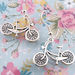 May include: A pair of silver bicycle earrings. Each earring features a detailed bicycle charm with a silver hook.