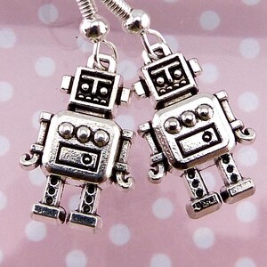 May include: A pair of silver-toned robot earrings. Each earring features a detailed robot design with a square head, circular body accents, and articulated limbs. The earrings hang from silver-colored hooks, perfect for a fun, quirky accessory.