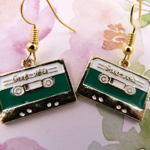 May include: Gold cassette tape earrings with a green background and white text that reads "Good Vibes".